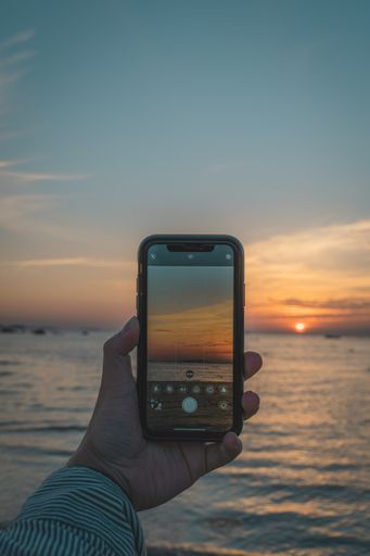 A person's hand holding a telephone and taking pictures of a beautiful sunset