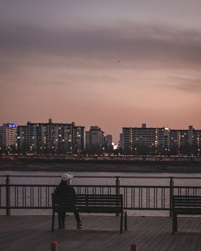 A female in a facial mask sitting on a bench and observing a beautiful sunset over the city