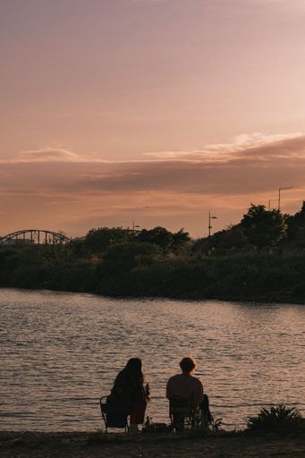A vertical shot of people sitting in a riverbank, talking and observing the beautiful view