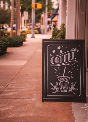 A coffee sign on a sidewalk near bushes
