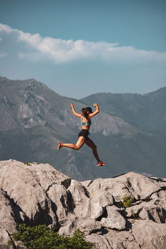 A woman athlete leaping over rocks atop a mountain