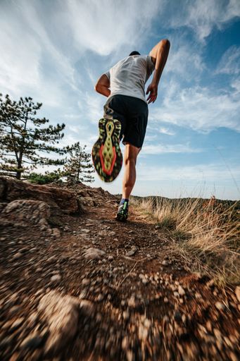 A man in athletic attire jogging on rocky terrain and grass under a picturesque sky