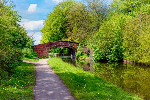 Historic brick bridge over serene English canal with lush trees on a bright spring day