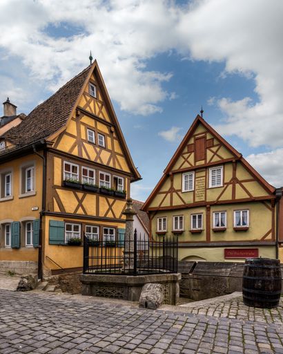 An old wooden barrel in front of the buildings of Plonlein in a cobblestone street at the daytime against blue, clear sky