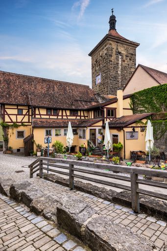 A vertical shot of an old stairway in a cobblestone street with a cafe's outdoor area and classic medieval building in the background at the daytime