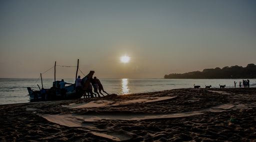 A group of individuals enjoy the sunset on the beach beside a boat