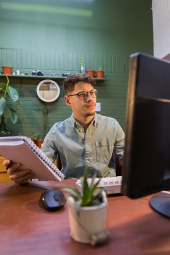 A young Hispanic male working on a computer holding a notebook