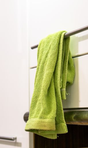 A vertical closeup green towel hanging messily on a bathroom bar