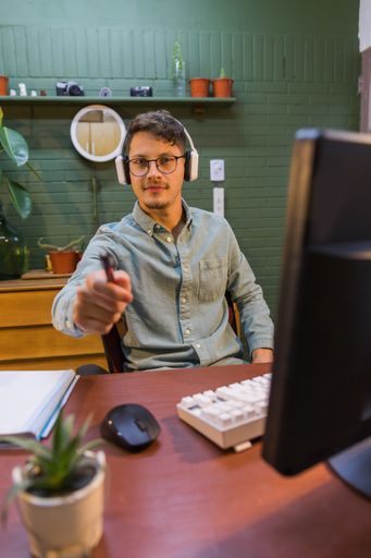 A young Hispanic male with headphones in front of the computer in the office handing a pencil