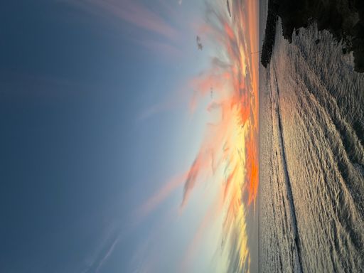 A dramatic sunset over the ocean with a lighthouse, clouds reflecting in the water