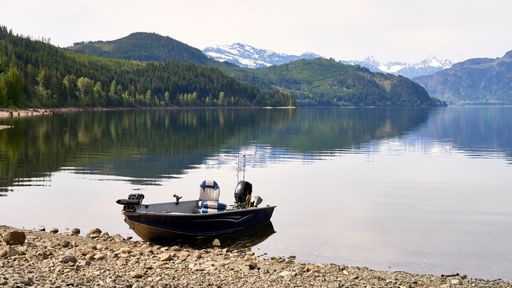 A small aluminum power boat with a motor at the edge of a beautiful lake with forests and snow covered mountains in the background.