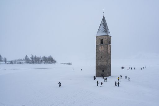 The bell tower stands prominently in the center of snow-covered Resia lake, surrounded by a serene winter landscape, Alto Adige, Italy