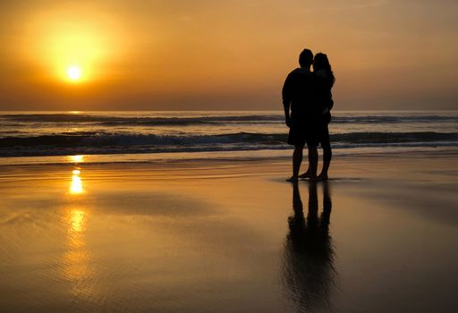 A silhouetted couple standing on beach at sunset, embracing each other