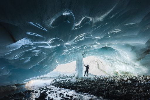 Winter landscape view of an alpinist exploring an ice cave with a frozen waterfall and a blue textured ceiling