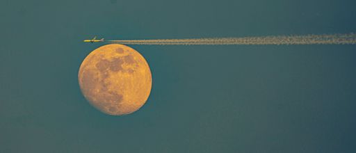 An airplane silhouetted against the day and night sky next to the moon