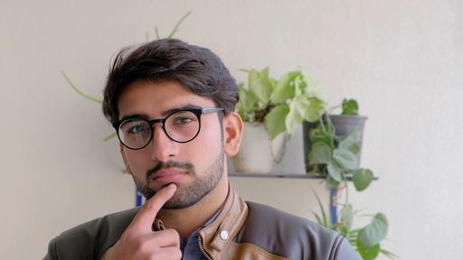A handsome Indian male pointing at his chin while looking at the camera with a  serious face