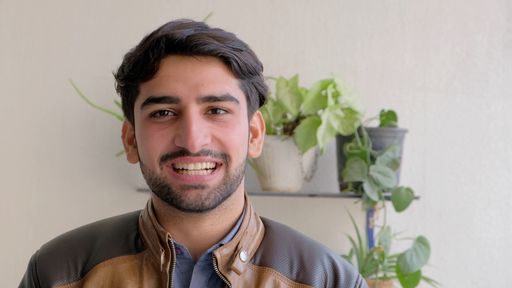 A view of an Indian guy in a leather jacket smiling in front of plants at home