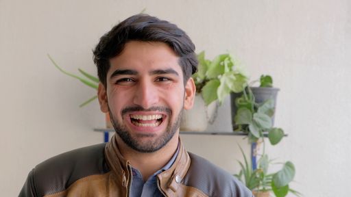 A happy smiling Indian male wearing a leather jacket with houseplants in the background