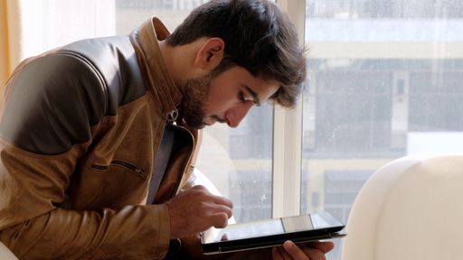 A view of an Indian guy in a leather jacket sitting down and looking at his tablet at home