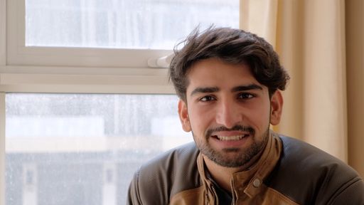 A handsome smiling Indian man looking at the camera against a wall with plants in pots