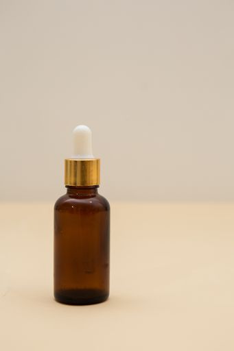 A vertical shot of a small serum bottle against a beige background