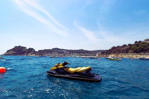 Fantastic shot of a wavy sea with a jet ski in front and many boats on mountains background of Tossa de Mar, in a summer day in the Mediterranean sea