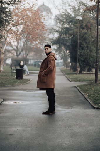 A man stands on a road surrounded by trees, his coat unbuttoned