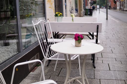 A closeup shot of a street cafe with white chairs and table and small vase of flowers