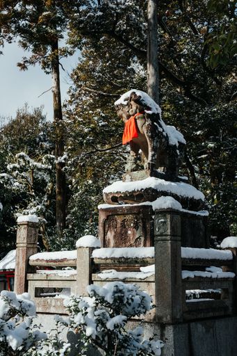 An Ancient style traditional Japanese statue covered in rare winter snow at Fushimi Inari Shrine in Kyoto Japan.