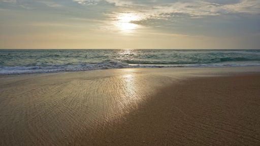 A mesmerizing seascape with a sandy beach under a cloudy sky at sunset