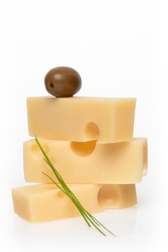 A vertical closeup shot of an olive on top of a stack of Swiss cheese slices on an isolated white background