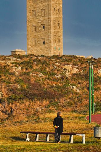 A vertical shot of a person standing in front of the Tower of Hercules in Coruna, Galicia, Spain