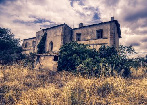 An old abandoned building in a field covered in the grass under a cloudy sky
