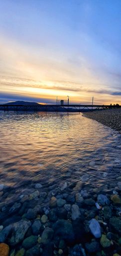 A vertical shot of stones on the shore of a lake during sunrise