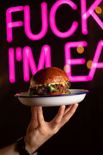 A vertical shot of a waiter holding a tray with a delicious beef burger with melted cheese on it in a cafe