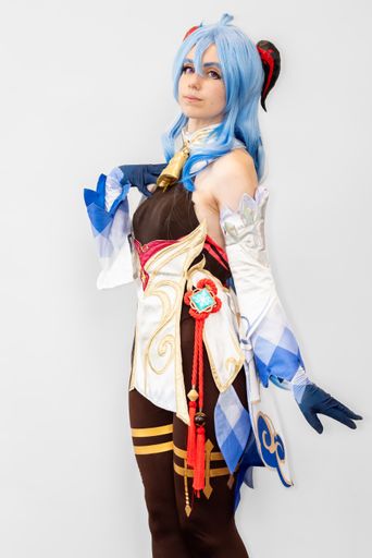A female cosplayer with blue hair and an elaborate dress posing against a neutral background