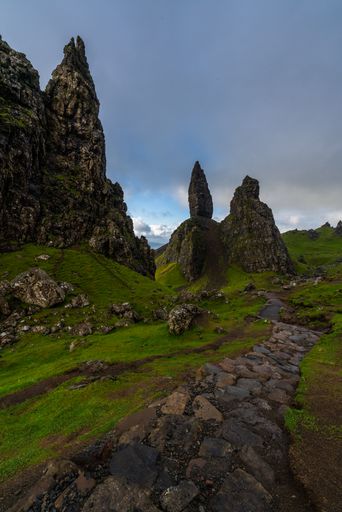 A Rocky terrain lining a dirt road with rocks under a cloudy sky