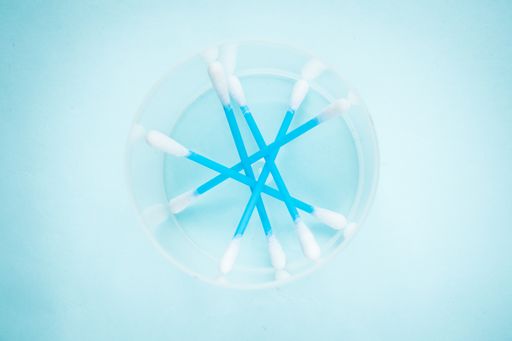 A plastic container with cotton swabs on a light blue surface