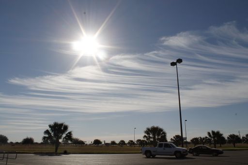 Two cars parked in a park parking lot with the Sun shining bright in the sky