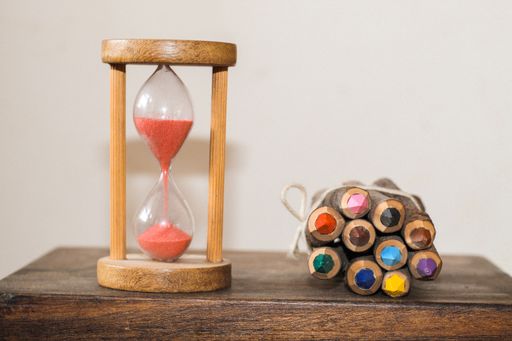 The colorful pencils and an hourglass on the table.