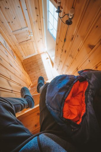 A vertical high angle shot of a person sitting on top of the stairs with a coat on his knees in a wooden cabin in Norway