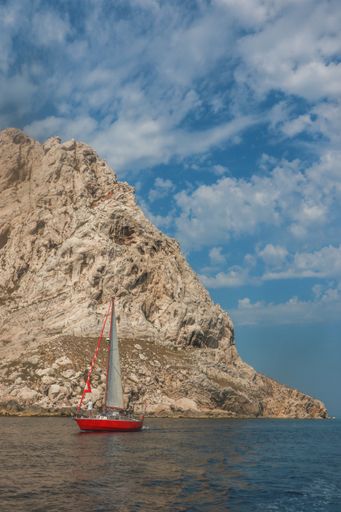A boat sails by a rocky hill on the water. Calanques, France