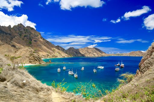 A landscape of sailing ships on the sea surrounded by rocky cliffs in Komodo National Park, Indonesia
