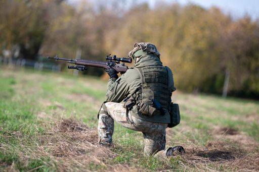 A man in camouflage crouches holding a rifle