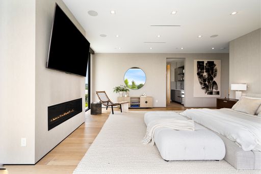 A Spacious bedroom with a large white bed, chair, fireplace, and a flat-screen TV