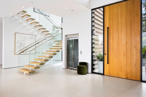 A room with stairs, a large door and an elevator inside a luxurious modern house with white walls