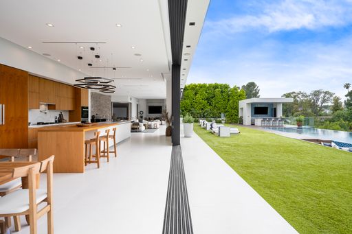A contemporary interior with a wooden table and expansive glass wall connected to a pool area