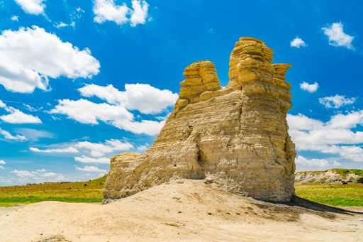 Three rock formations on grass and dirt under a blue sky with fluffy white clouds