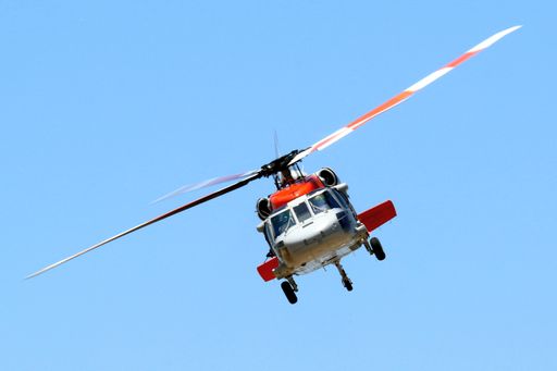 A red and white helicopter flying in a clear blue sky