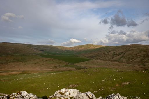 A scenic view of rolling hills and green fields under a partly cloudy sky in Skipton, England